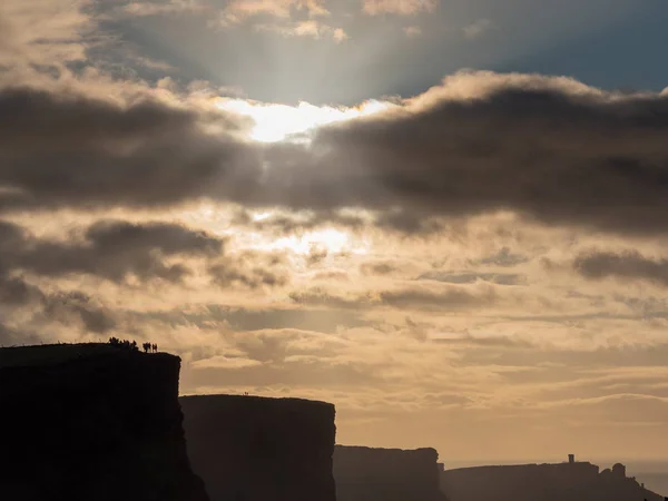 Cliff of Moher silhouet en toeristen, humeurig hemel, zon flare en stralen. County Clare, Ierland. — Stockfoto