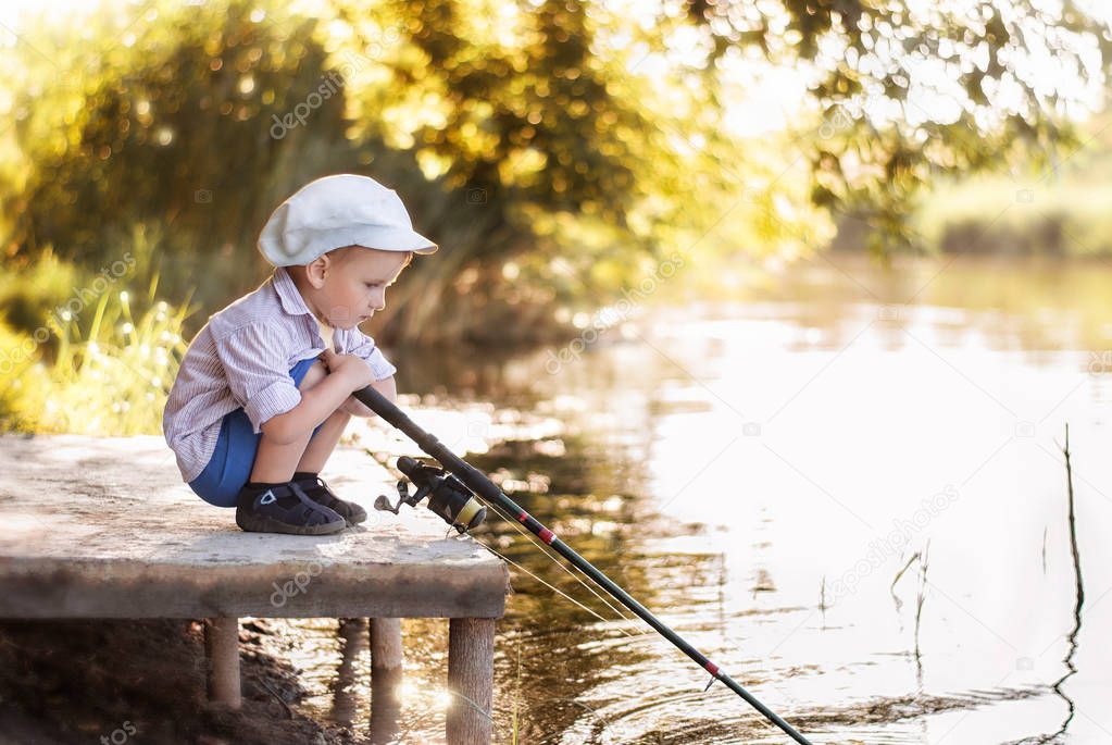 Little boy is fishing at sunset on the river