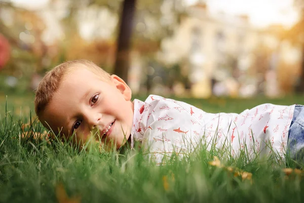 Улыбающийся маленький мальчик лежит на зеленой траве — стоковое фото