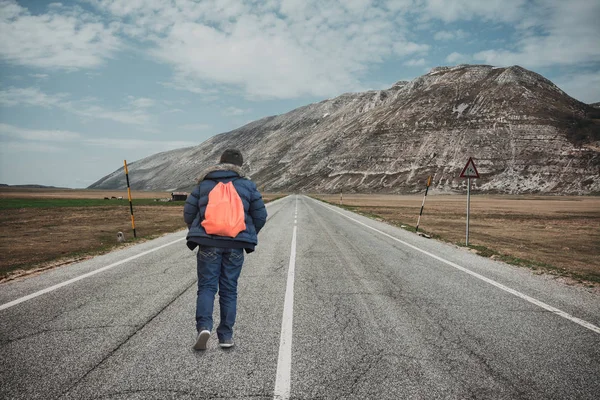 Teenager walking away on mountain road. Concept of escape and adventure