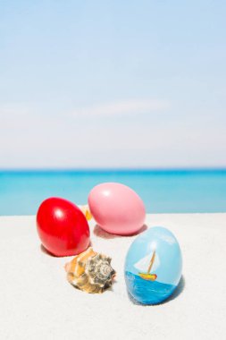 Tropikal plaj, dikey Paskalya'da. Yumurta beyaz kum üzerinde. Bahar tatil ve seyahat kavramında