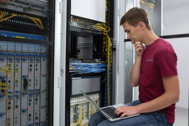 Büyük veri merkezindeki bir dizüstü bilgisayarda erkek sunucu mühendis çalışıyor.