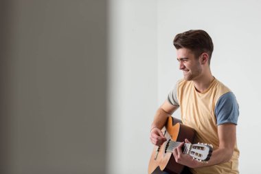 Oldukça genç adam ışık oturma odasında kanepede otururken gitar çalmak