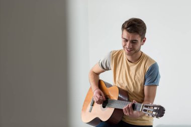 Oldukça genç adam ışık oturma odasında kanepede otururken gitar çalmak