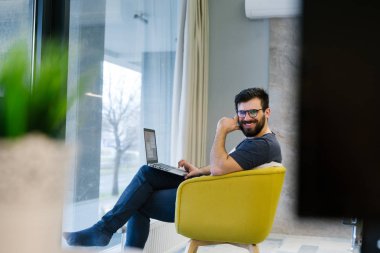 Göz gözlük takan ve modern lightful ofiste dizüstü kullanarak tshirt sakallı adam. Horizontal.Blurred arka plan