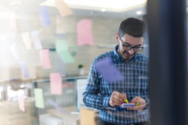 Businessman sticking notes to share idea. Brainstorming concept. Sticky notes on glass wall. clipart