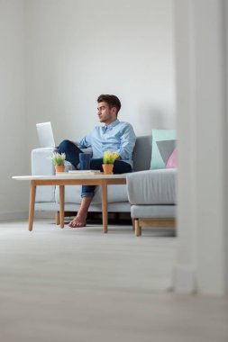 Genç, çekici, gülümseyen adam bilgisayarına bakıyor.