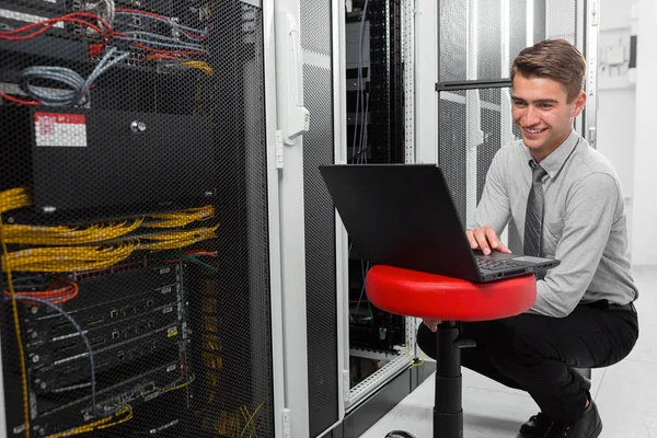 Male Server Engineer Works on a Laptop in Large Data Center.