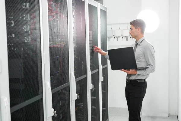 Büyük veri merkezindeki bir dizüstü bilgisayarda erkek sunucu mühendis çalışıyor.