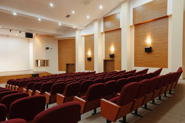 Large empty lecture hall with red chairs.