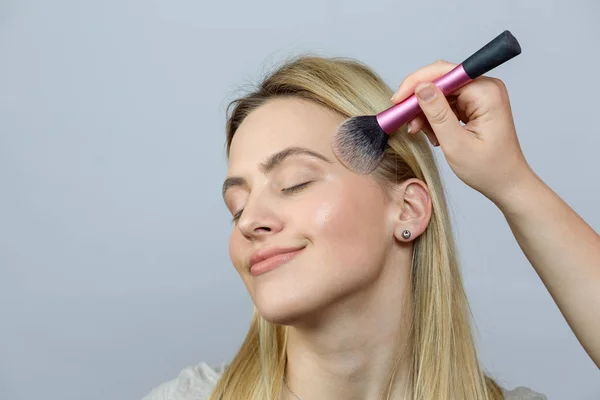 beautiful woman holding makeup brush over gray background