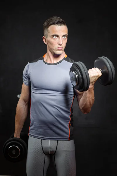 young male fitness model holds the dumbbell