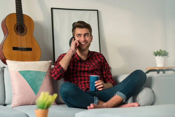 man talking on the mobile phone and smiling while lying on couch