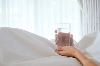 Asya kadın kopya alanı f ile beyaz yatakta su bardağı tutan