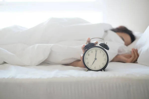Egy nő alszik az ágyon, kikapcsolja az ébresztőórát. — Stock Fotó