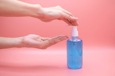 El dezenfektanı jel pompası kullanan kadın elleri. Pompa şişesindeki temizleyici mikropları, bakterileri ve virüsü öldürmek için, pembe arka plan.