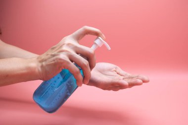 El dezenfektanı jel pompası kullanan kadın elleri. Pompa şişesindeki temizleyici mikropları, bakterileri ve virüsü öldürmek için, pembe arka plan.