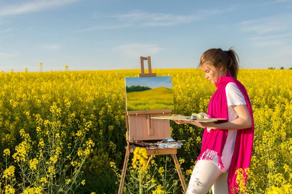 girl painter with an easel in a yellow rapeseed field