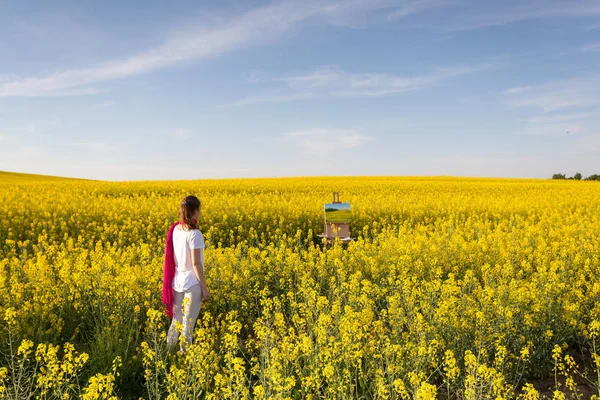 girl painter with an easel in a yellow rapeseed field
