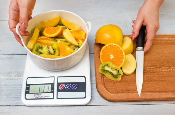 Ağırlığında bir aşçı kadın elinde bir terazi tartı ve bir bıçak, taze meyve ile kesme tahtası üzerinde tutan meyve dilimlenmiş. Sağlıklı yaşam ve yemek, pişirme ve kavram Diyet.