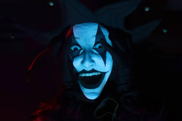 Horrible screaming jester\'s face in dark room, close-up.