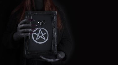 Üzerinde pentagram sembolü olan büyü sihirli kitabı tutan uzun pençeleri olan bir cadının elleri. Cadılar Bayramı, kara büyü kavramı.