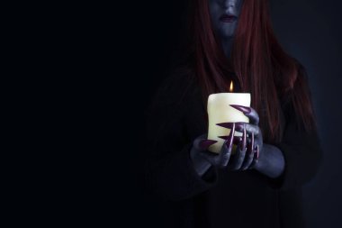 Uzun kızıl saçlı ve yanan bir mum tutan uzun keskin pençeleri ile Cadı, kopya alanı ile fotoğraf. Cadılar Bayramı, kara büyü kavramı.