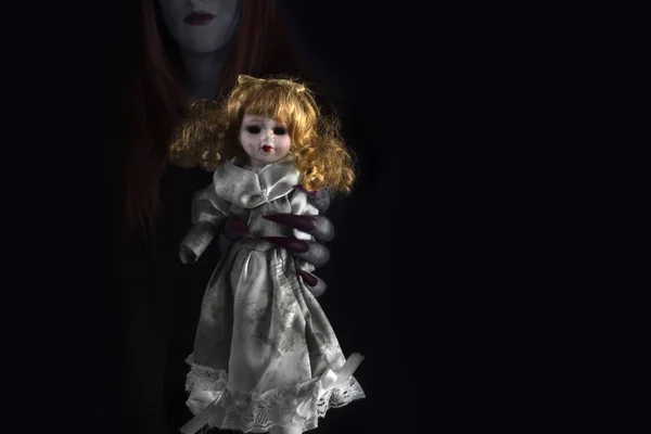 Uzun keskin pençeleri olan bir cadının elleri ve ürpertici kirli porselen bir bebek. Cadılar Bayramı, kara büyü kavramı.