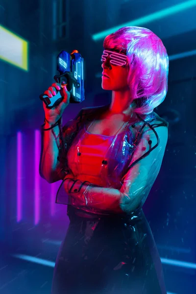 Cyberpunk Mujer Pelo Rosa Gafas Neón Impermeable Transparente Sosteniendo Arma —  Fotos de Stock