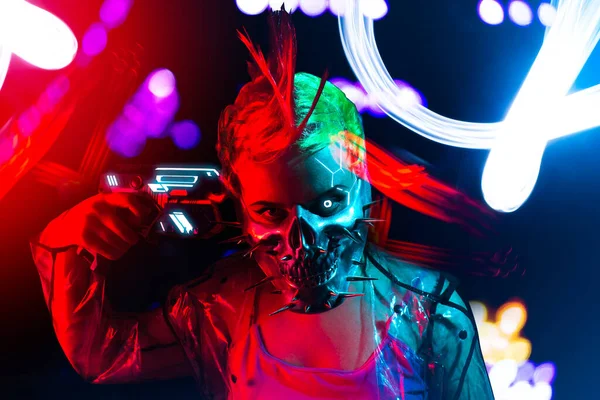 Crazy cyborg woman with mohawk hairstyle in spiked mask putting a gun to her head.