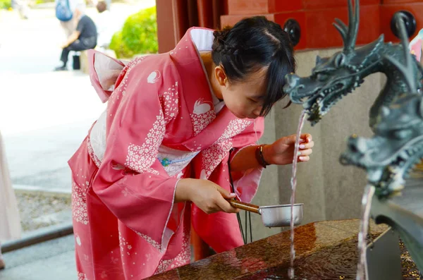 Tokyo, Japonya - 28 Mayıs 2018: Sensoji Budist tapınağını girmeden önce bir tören arıtma ritüel bir parçası olarak Japon kimono içme suyu bir Chozuya giyen genç kız. 
