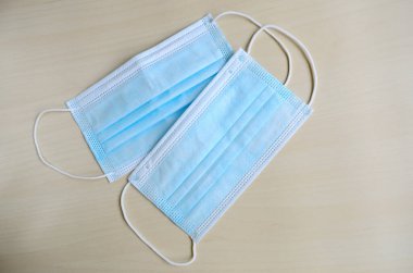 Ahşap arka planda izole edilmiş plastik kulaklıklı cerrahi maske. Ağız ve burnu örtmek için tipik 3 katlı cerrahi maske. Koruma kavramı.