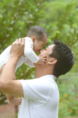 Babalar günün kutlu olsun! Neşeli genç baba, açık hava parkında sevimli oğluna sarılıyor..