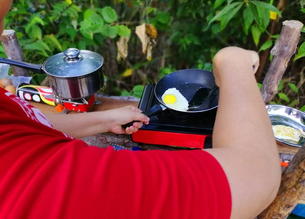 Woman cooking breakfast on campfire in cast iron pan with selective focus.