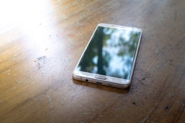 Akıllı telefon parlak güneşli bir günde ahşap bir masada.