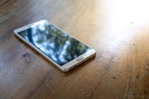 The smart phone is on a wooden table on a bright sunny day.