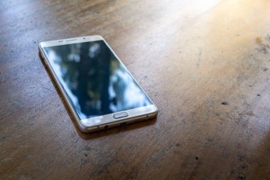 Akıllı telefon parlak güneşli bir günde ahşap bir masada.