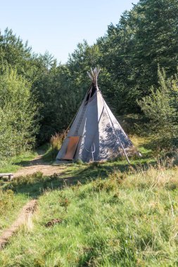 Yaz boyunca Karpatlar 'da güneşli bir ormanlık arazide duran geleneksel çadır, yemyeşil ve dağ manzaralarıyla çevrili, doğa ve doğa ile uyumu sembolize ediyor..