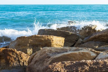  Kıbrıs kıyı şeridinin deniz kenarındaki kayalara çarpan dalgalarla manzarası, doğal ışık altında dinamik sıçramalar ve deniz spreyi yaratarak Akdeniz kıyısının saf güzelliğini gözler önüne seriyor.
