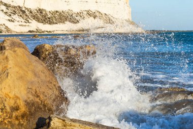  Kıbrıs kıyı şeridinin deniz kenarındaki kayalara çarpan dalgalarla manzarası, doğal ışık altında dinamik sıçramalar ve deniz spreyi yaratarak Akdeniz kıyısının saf güzelliğini gözler önüne seriyor.