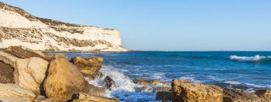  Kıbrıs kıyı şeridinin deniz kenarındaki kayalara çarpan dalgalarla manzarası, doğal ışık altında dinamik sıçramalar ve deniz spreyi yaratarak Akdeniz kıyısının saf güzelliğini gözler önüne seriyor.