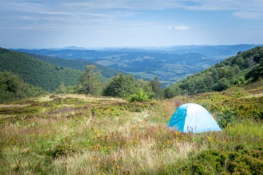  Yaz boyunca Karpatlar 'da yeşil bir çayırda kurulan mavi çadır, dağların manzaralı manzarası, macerayı sembolize ediyor, aktif turizm ve doğada dinlenmeyi.