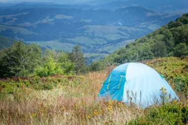  Yaz boyunca Karpatlar 'da yeşil bir çayırda kurulan mavi çadır, dağların manzaralı manzarası, macerayı sembolize ediyor, aktif turizm ve doğada dinlenmeyi.