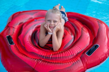 Güzel çocuk bir hava şiltesi üzerinde oturur ve tatilde yaz aylarında açık bir gölette yüzer