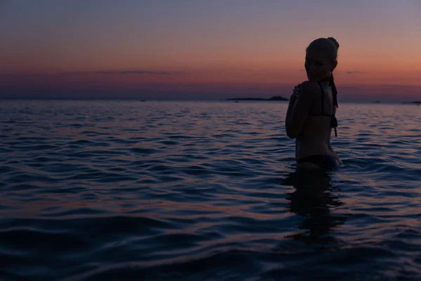 Mujer tierna se encuentra en la playa al atardecer brillante en el mar cálido con una silueta —  Fotos de Stock