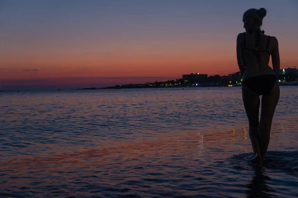 Sexy bella donna si trova sulla spiaggia al tramonto arancione nel mare caldo con silhouette — Foto Stock