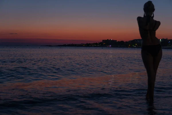 Donna insaziabile si trova sulla spiaggia al tramonto luminoso nel mare caldo con silhouette — Foto Stock