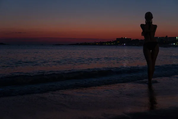 Ragazza sexy si trova sulla spiaggia al tramonto nel mare con una silhouette — Foto Stock