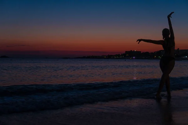 Insaziabile bella si erge sulla spiaggia su una nebbia fioca dal tramonto in un mare caldo con una silhouette — Foto Stock