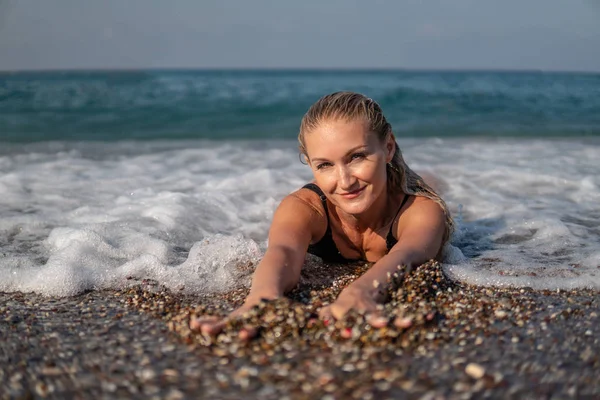 Una bella donna si trova sulla riva dell'oceano e ascolta il surf liscio delle onde, gode di una giornata estiva, al sole più luminoso — Foto Stock